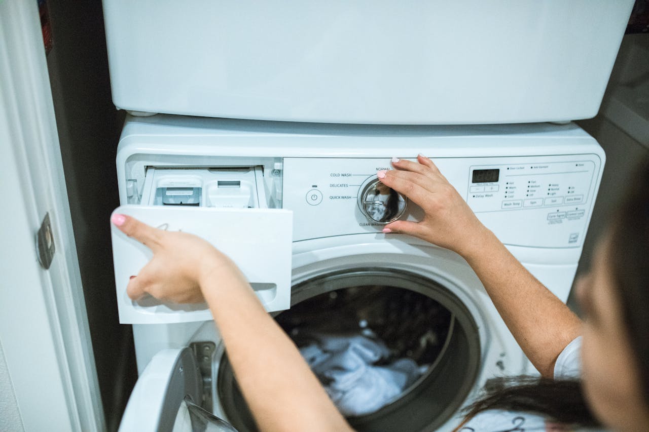 services-01 A person in a laundry room adjusting settings on a washing machine.